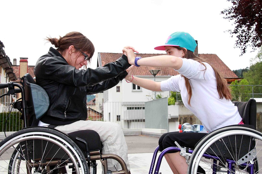 Zwei Mädchen begegnen sich im Rollstuhl
