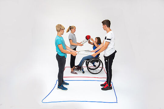 Quatre élèves déplacent par deux une boule sur une feuille de papier. Une élève est en fauteuil roulant.