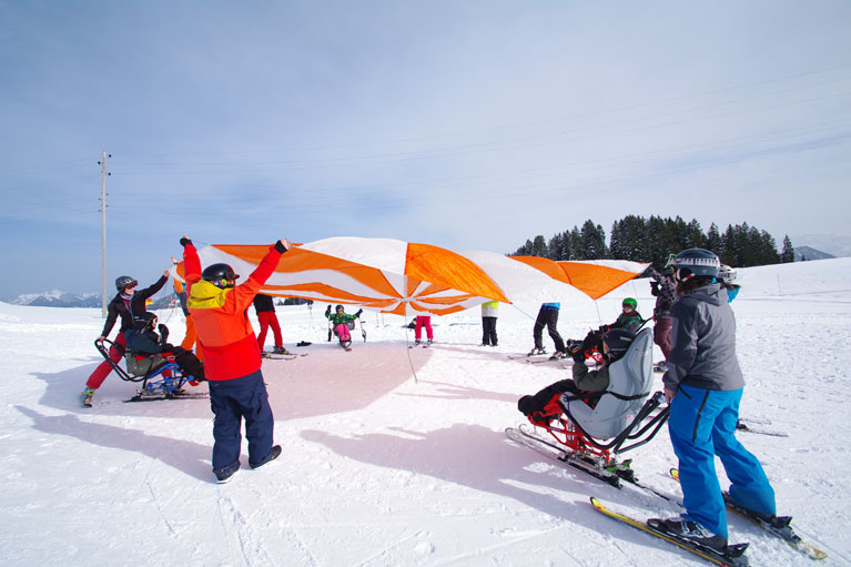 Sitzende und stehende Skifahrer spielen mit einem Schwungtuch im Schnee