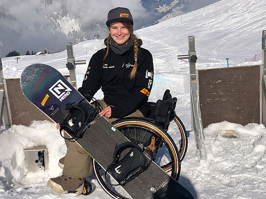 Romy besucht regelmässig die Fördertrainings von PluSport. Romy im Rollstuhl mit ihrem Snowboard.