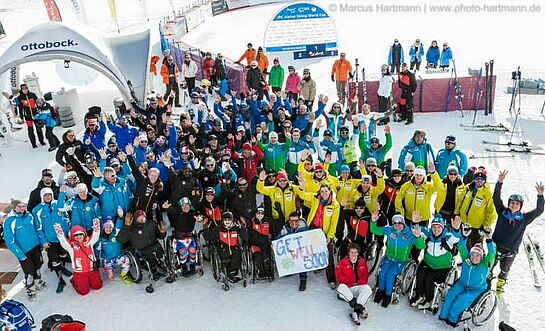 Aktive und passive Sportler, Leiter, Volunteers und viele mehr werden zum Sympathiemitglied von PluSport Gruppe von vielen Athleten stehen im Schnee und winken
