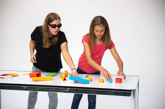 Zwei Schülerinnen verteilen Papierformen auf dem Tisch.