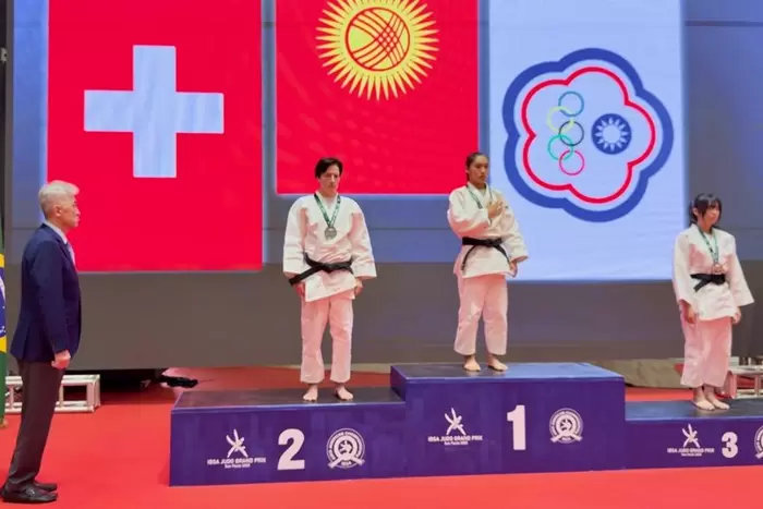 Drei Judosportlerinnen stehen auf einem Podium mit Medaillen. Die Athletin in der Mitte steht auf dem obersten Podest, während die beiden anderen auf dem zweiten und dritten Platz stehen. Im Hintergrund sind Nationalflaggen zu sehen.