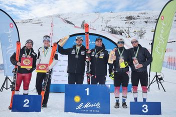 Fünf männliche Skifahrer stehen auf einem verschneiten Podium mit Medaillen und Preisen und feiern den Sieg bei einem Skirennen. Der Sieger steht in der Mitte auf Podium 1, flankiert von den Zweit- und Drittplatzierten, mit verschneiten Bergen und Bannern im Hintergrund.