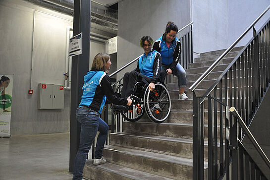 Kein Lift? An der Kadertagung wurde mit Rollstuhl geübt. Zwei Helferinnen üben mit einer Person im Rollstuhl auf der Treppe.