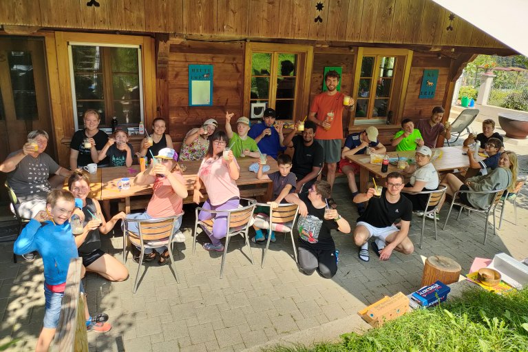 Eine Gruppe von Camp-Teilnehmenden und Leitenden sitzen zusammen im Schatten und trinken ein erfrischendes Getränk.