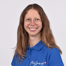Eine Frau mit langen hellbraunen Haaren und Brille lächelt in die Kamera. Sie trägt ein blaues Hemd mit Kragen und dem Aufdruck „Plysport“. Der Hintergrund ist schlicht und hell.