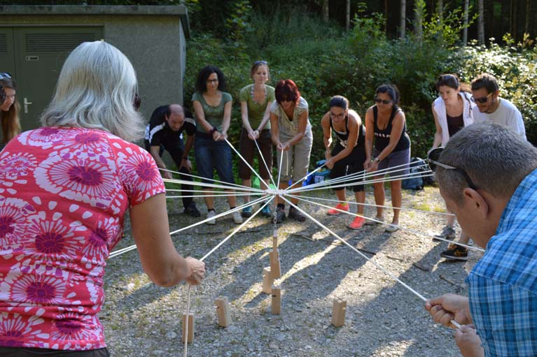 Eine Gruppe steuert Holzbauteile mit Seilen und versucht, einen Turm zu bauen