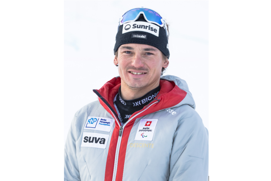 Ein lächelnder Sportler, der eine graue Schweizer Paralympics-Skijacke und eine schwarze Mütze mit dem Sunrise-Logo trägt.