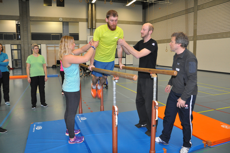 Un moniteur de la formation polysport sécurise l’apprenant sur les barres 